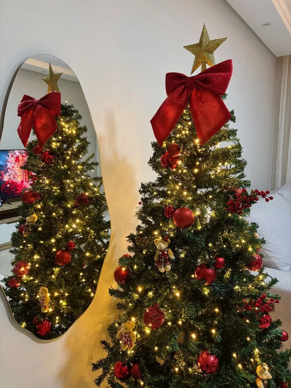 Árvore decorada com laço vermelho, estrela e luzes diante de espelho